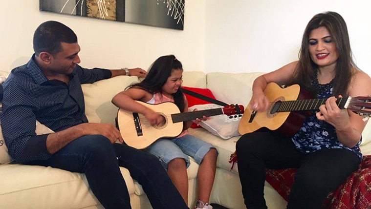 The Foneska family - Angelo, Eliza, Shanoline - sitting on a couch playing guitars.