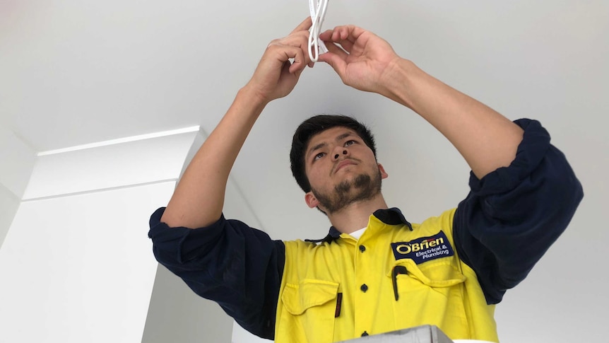 Ali Maisam works on some wires while standing on a ladder in a house.