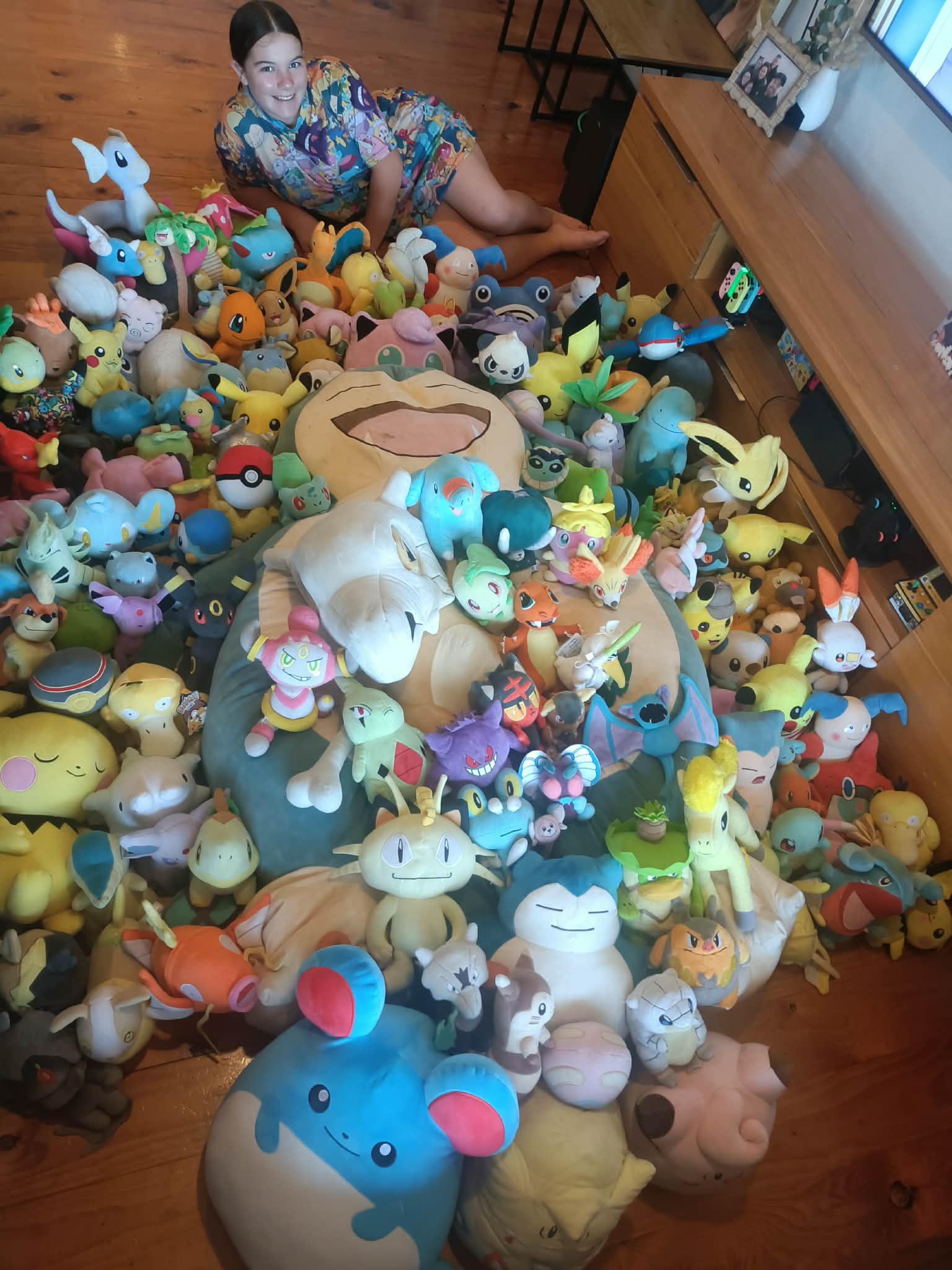 Una niña sentada rodeada de más de 100 peluches Pokémon.