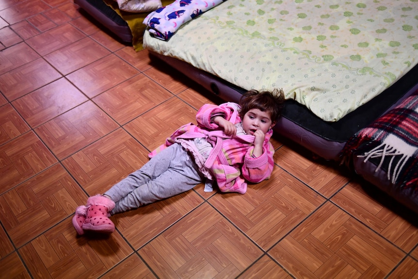 A young child lies on the floor next to an air mattress.