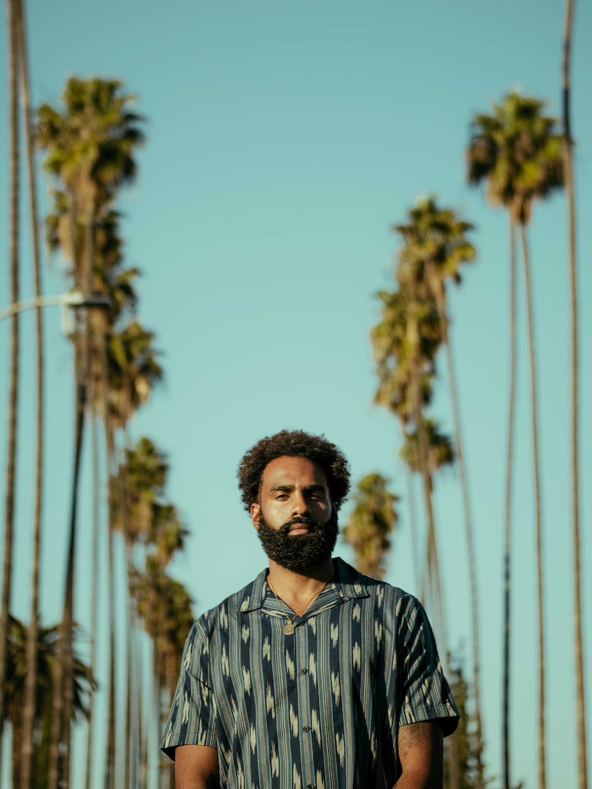 A man walks with blue sky and palm trees in the background.