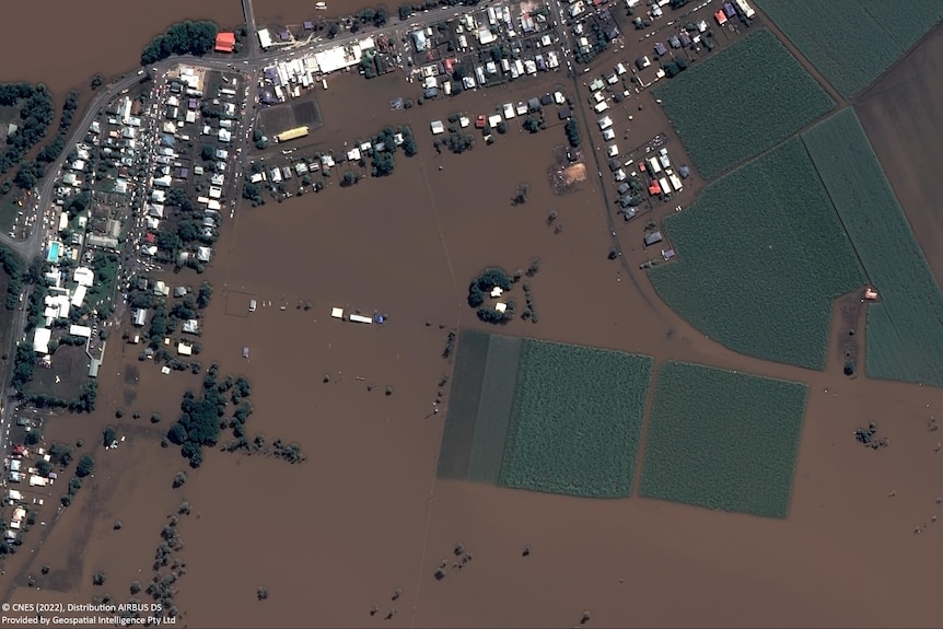 Aerial of flooded town surrounded by brown flood water. 