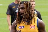A mid shot of Nic Naitanui walking on an oval wearing a yellow West Coast Eagles training jersey.