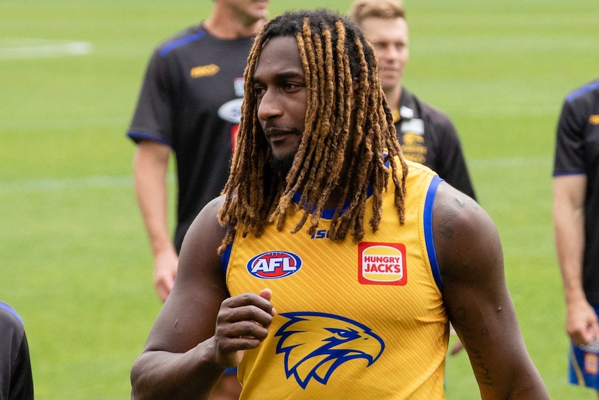 A mid shot of Nic Naitanui walking on an oval wearing a yellow West Coast Eagles training jersey.