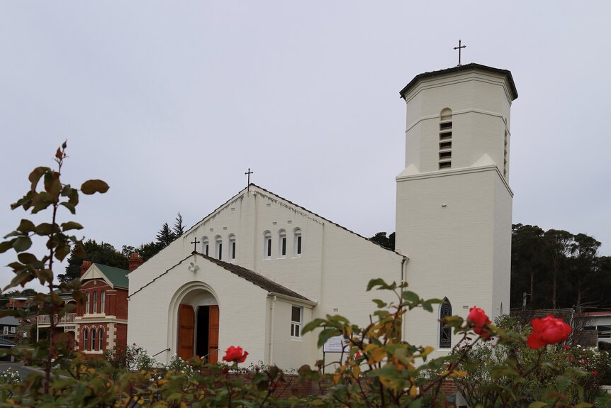 A white brick Spanish-style church with roses in the foreground
