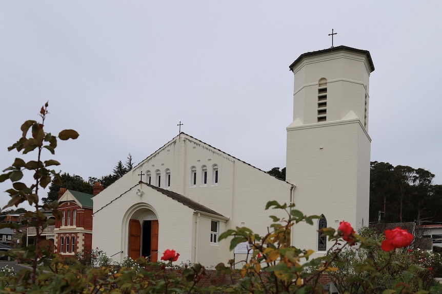 A white brick Spanish-style church with roses in the foreground