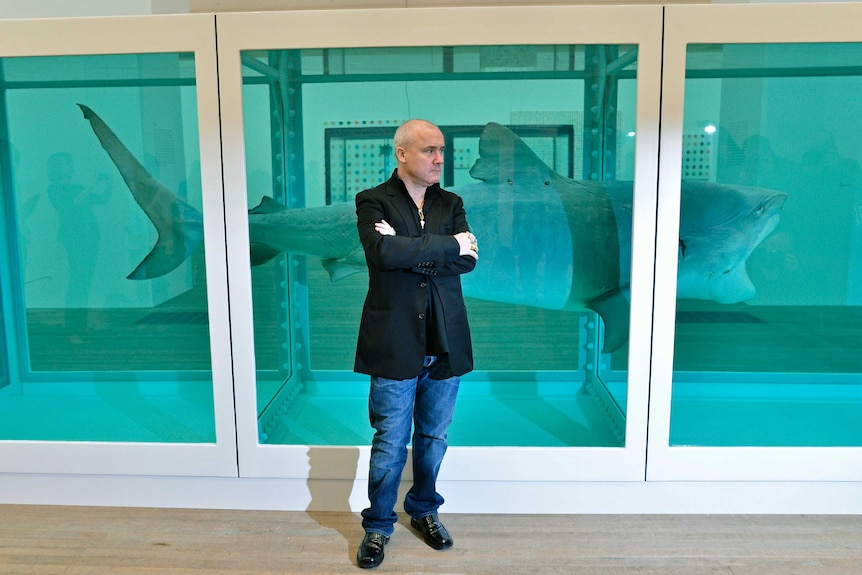 Damien Hirst poses next to a shark preserved in formaldehyde