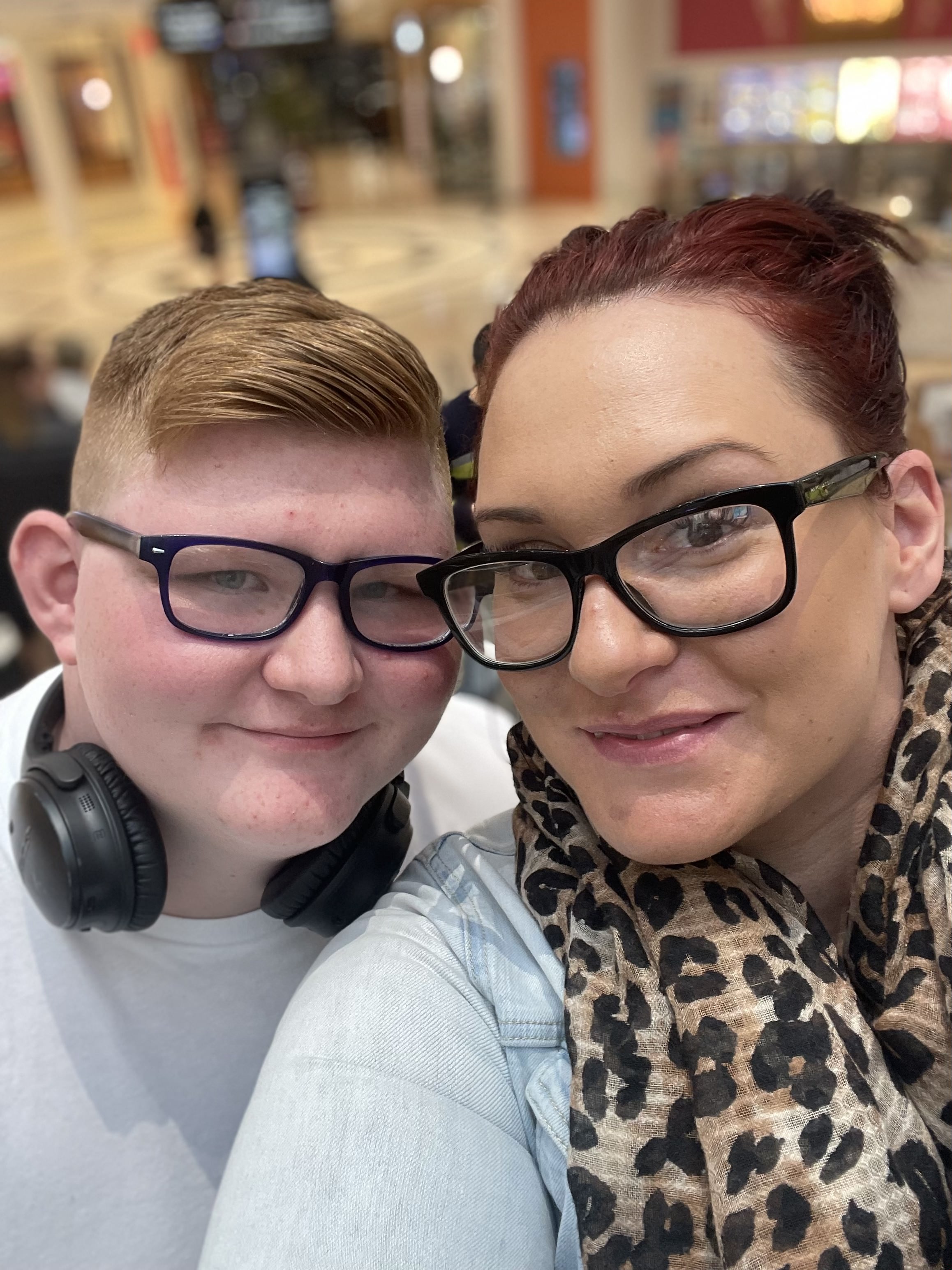 A boy with headphones around his neck poses for a photo with his mother.