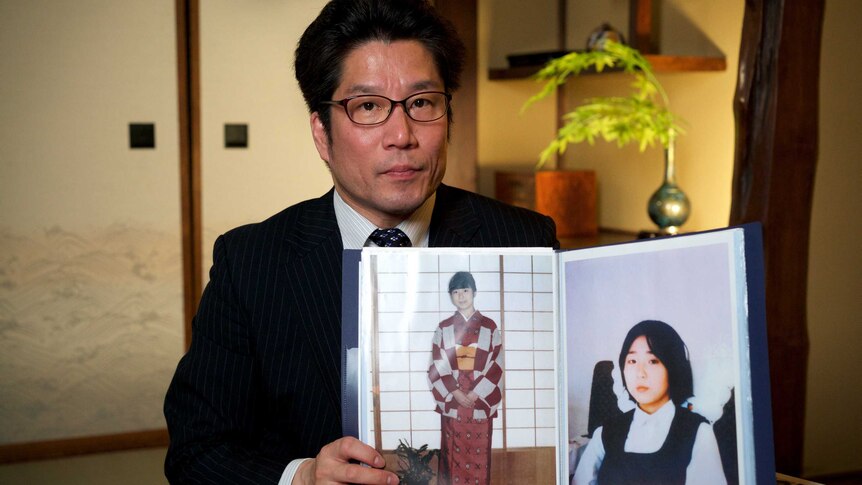 A man in a suit holds open a photo album featuring images of a young Japanese girl
