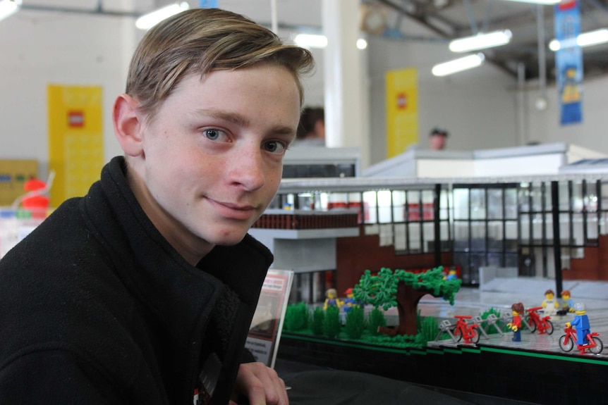 Connor leaning on a table of his creations. He is smiling.