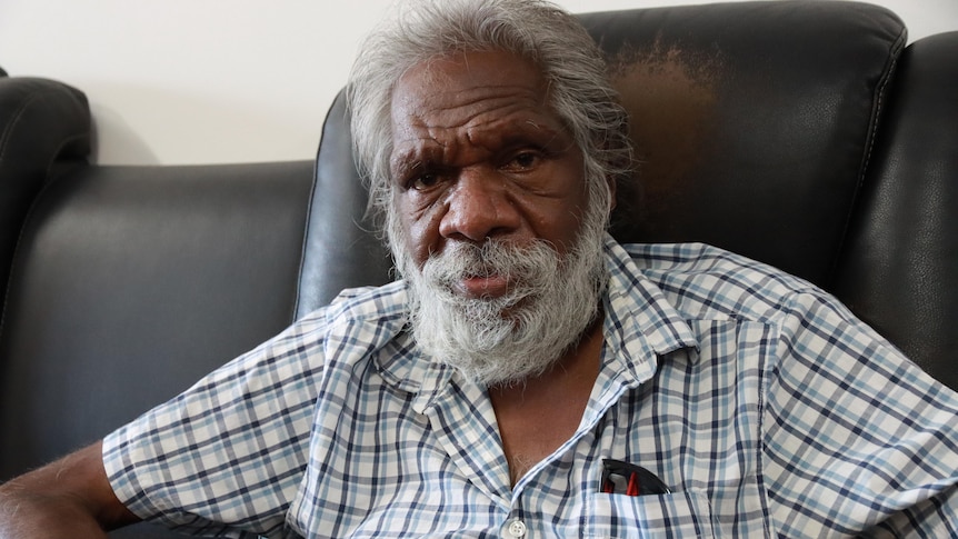 An Aboriginal man sits in a large black armchair. 