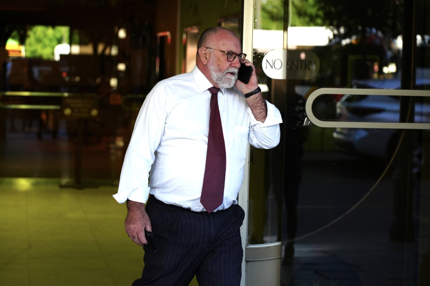 A man wearing a white shirt and red tie on his mobile phone outside court. 