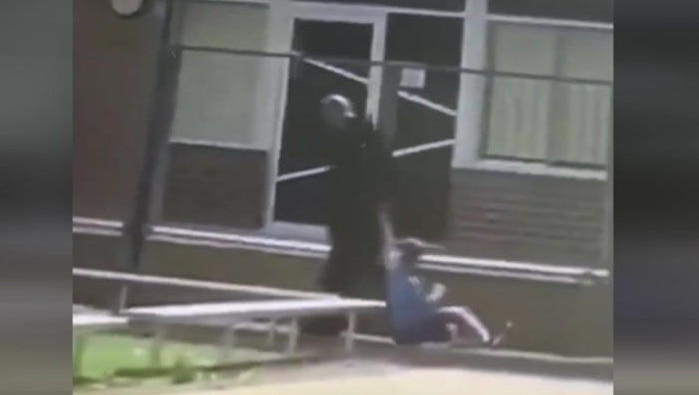 A man is shown dragging a boy through a school playground by his arm in a still from a video.