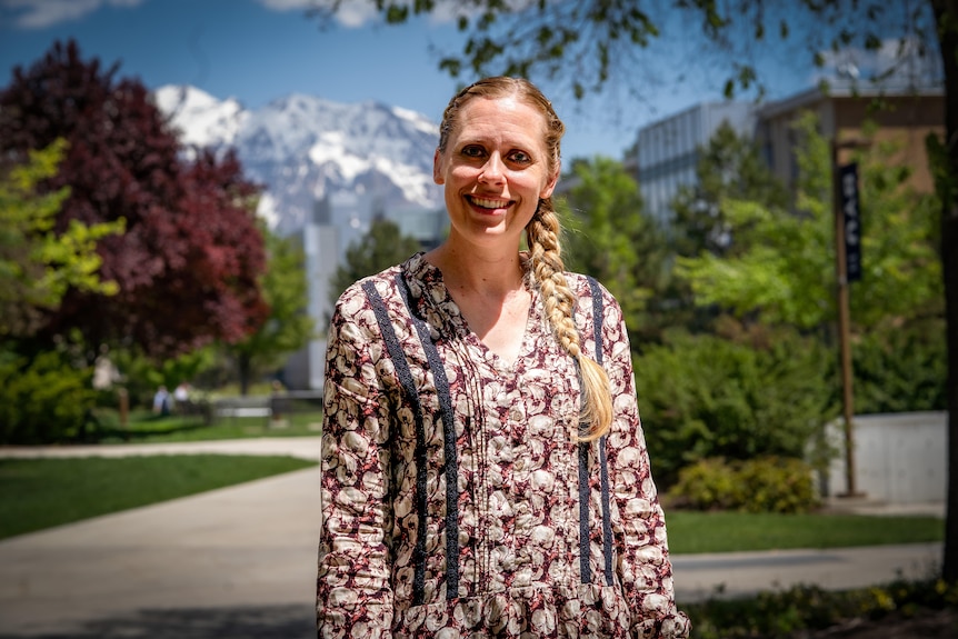 A woman with a long blonde plait stands with a snow-capped mountain behind her