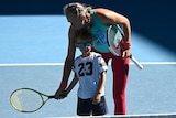 A female tennis player helps her son hold a racquet on the court.