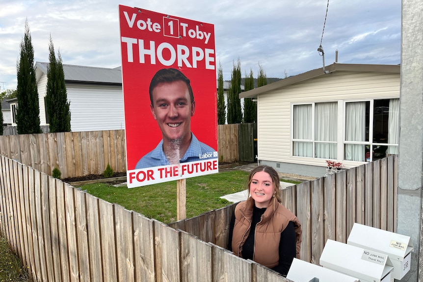 A woman with an election sign in the backyard.