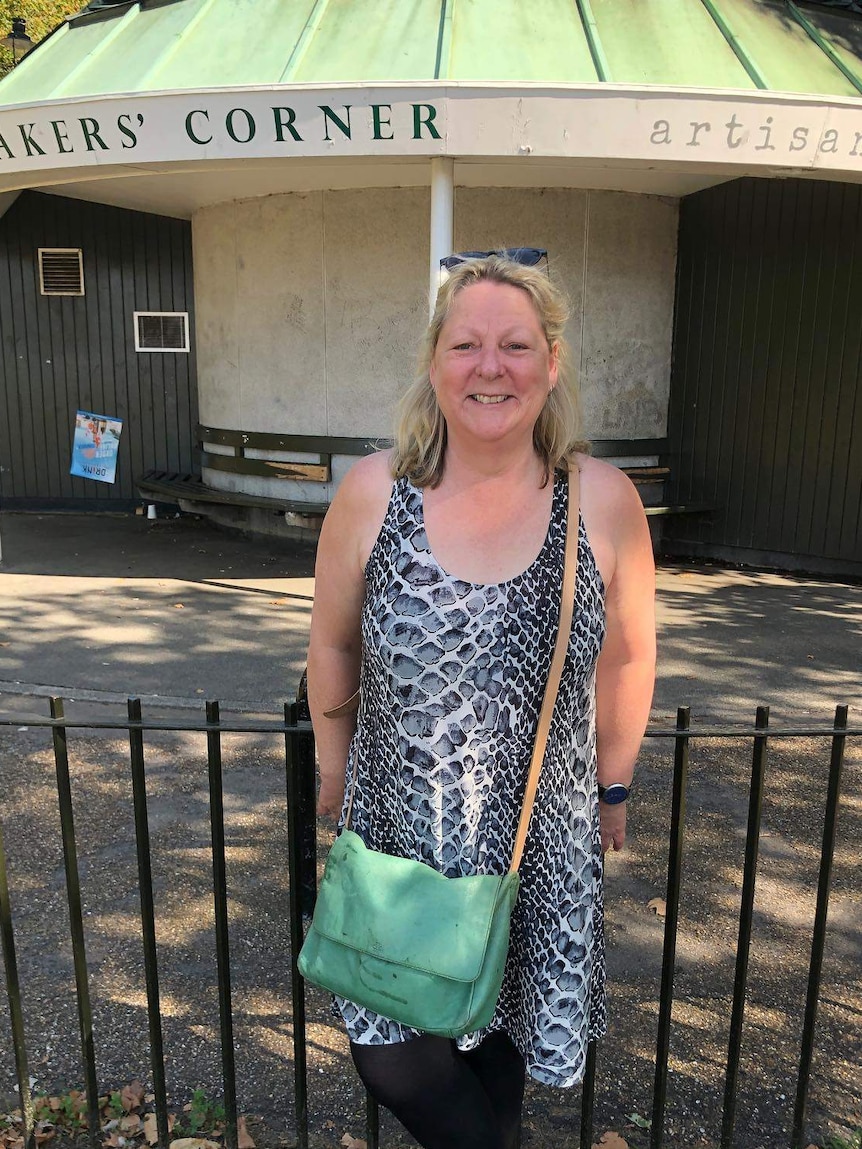 A middle-aged woman stands in front of a fence and smiling at the camera.