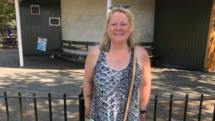 A middle-aged woman stands in front of a fence and smiling at the camera.