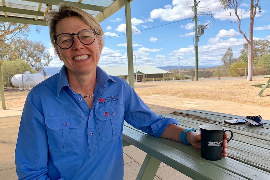 A woman in a blue, long-sleeved shirt sits at a table with a cup of tea.