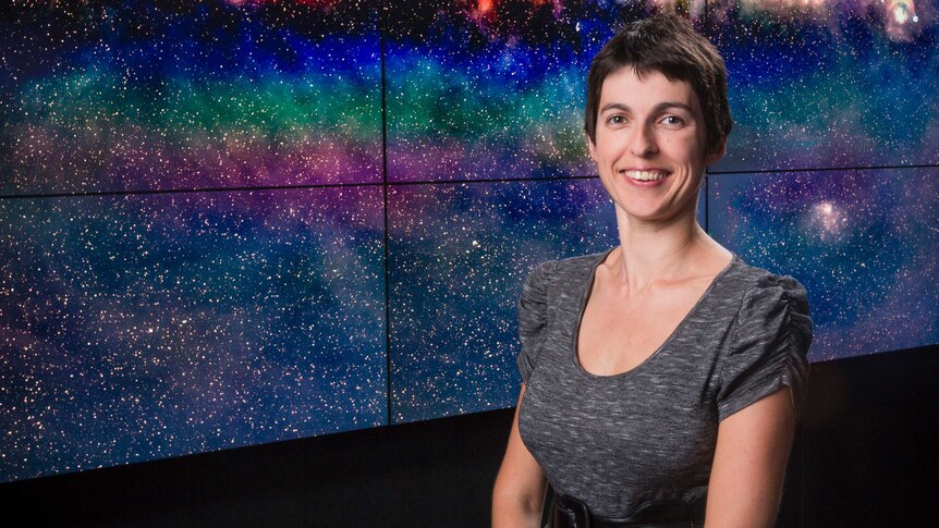 A woman standing in front of a rainbow coloured view of stars.