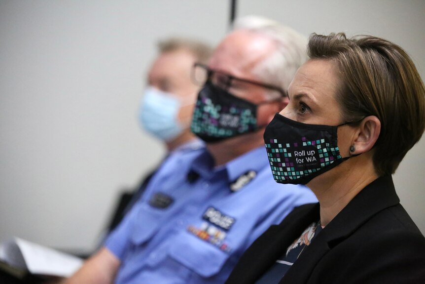 Amber-Jade Sanderson sits next to the Police Commissioner, both wearing masks.