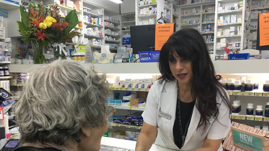Pharmacist Caroline Diamantis speaks to an elderly client with her back to us