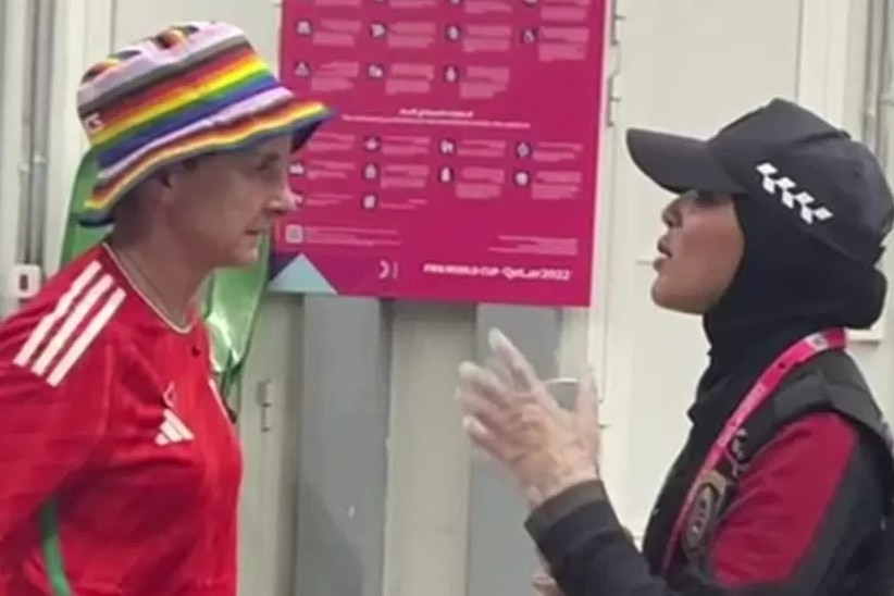 A woman wearing a red soccer jersey and rainbow hat speaking to another woman dressed in black