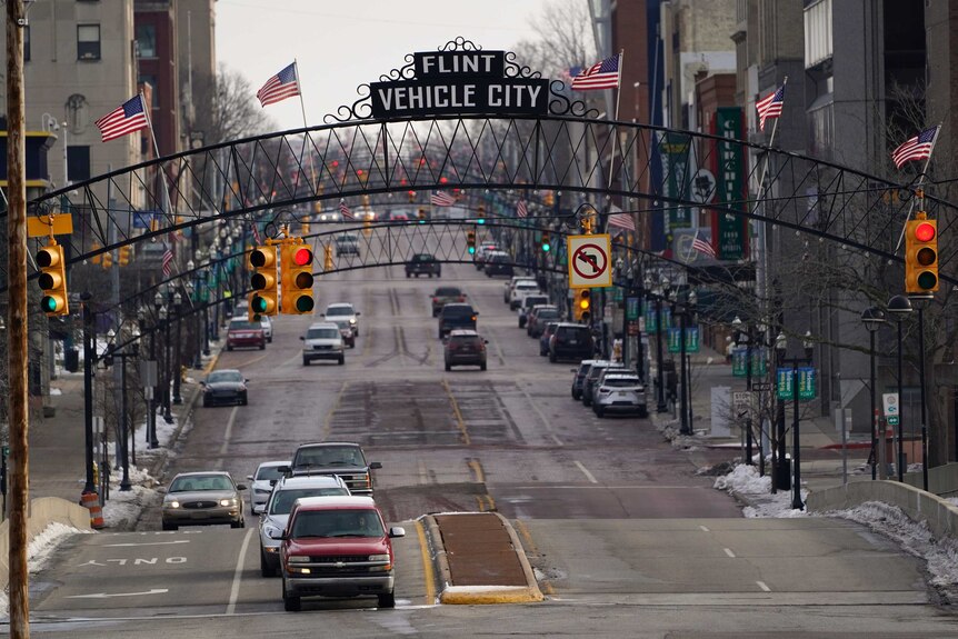 Vehicles drive through downtown Flint below a sign saying Flint Vehicle City.