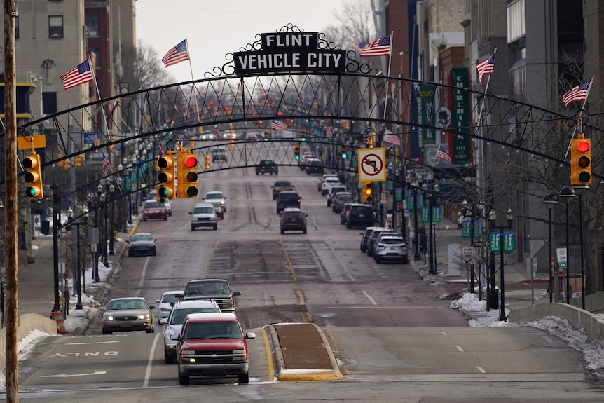 Vehicles drive through downtown Flint below a sign saying Flint Vehicle City.