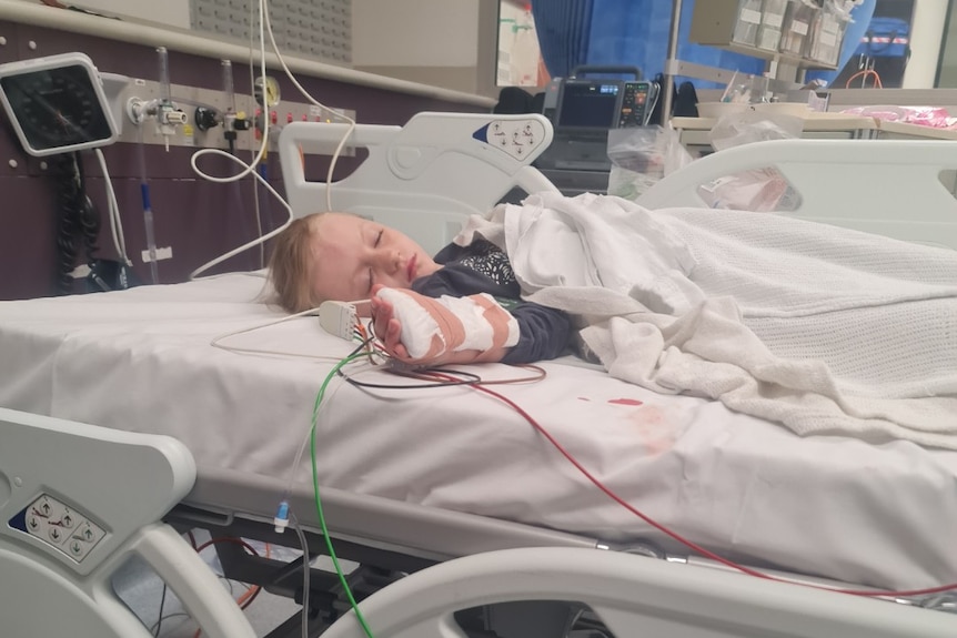 A young girl asleep in a hospital bed with tubes attached to her arm