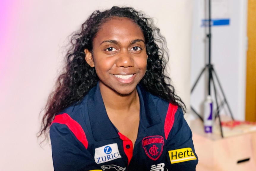 A young women with black curly hair smiles at the camera