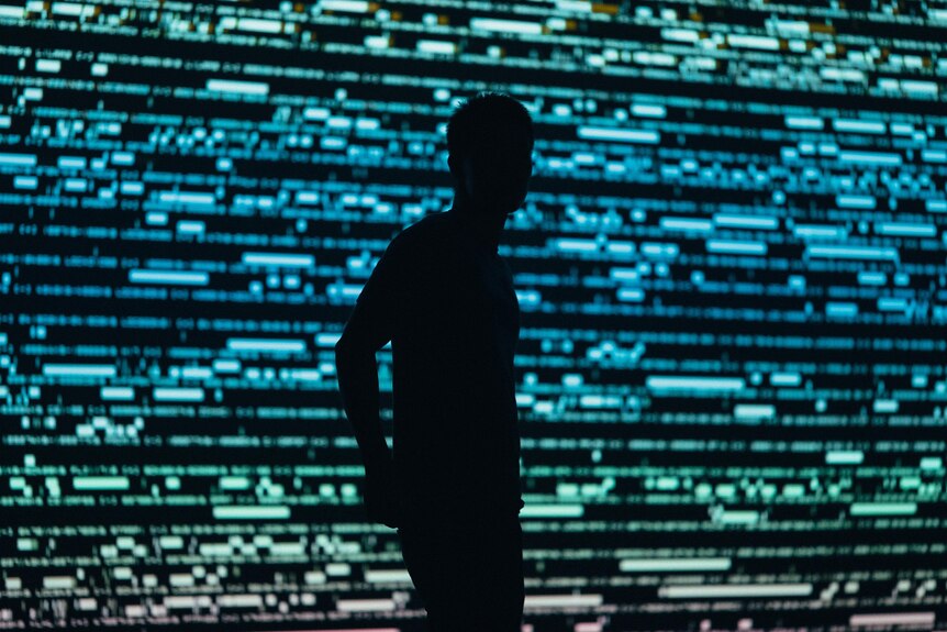 The silhouette of a man in front of a wall of digital characters/screens