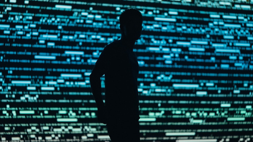 The silhouette of a man in front of a wall of digital characters/screens