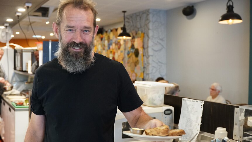 A man with a beard holding a plate with food in a cafe kitchen