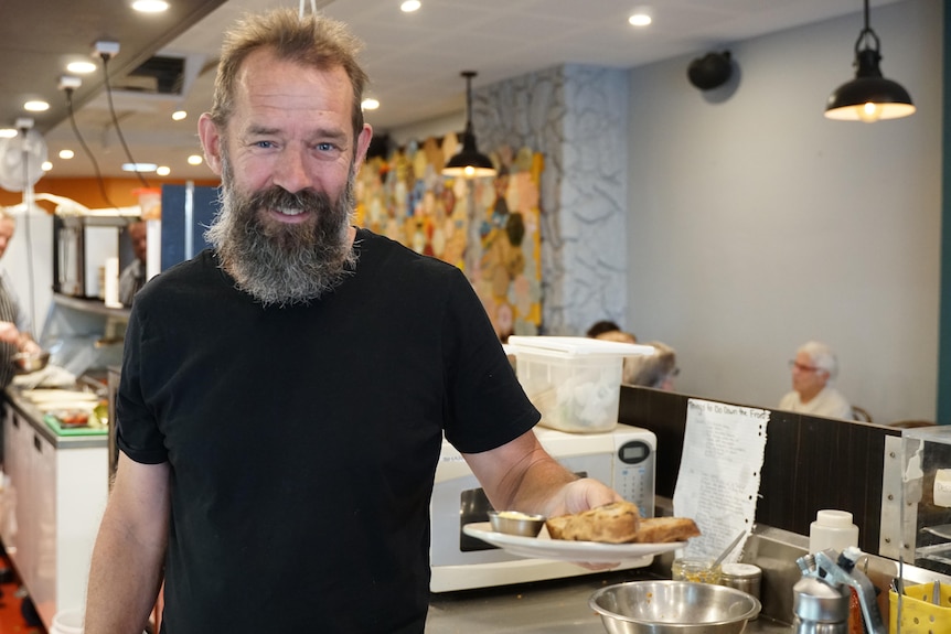 A man with a beard holding a plate with food in a cafe kitchen