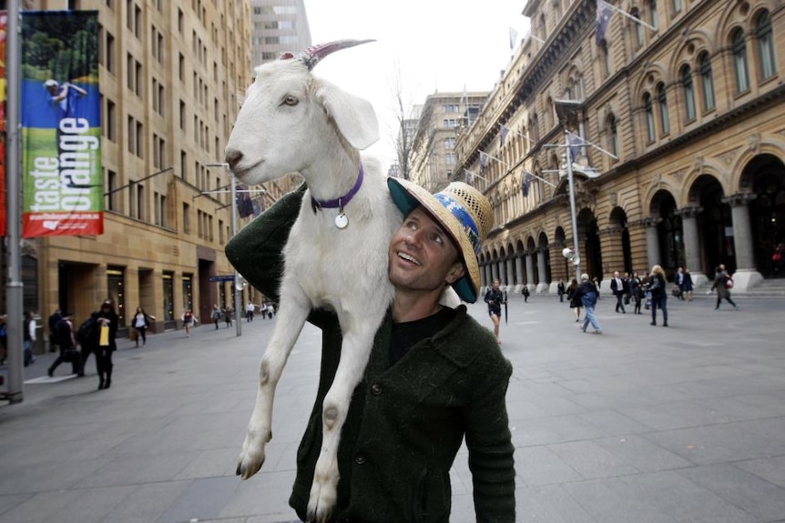 Jimbo Baboozi hold Gary the Goat over his shoulder while walking down the street