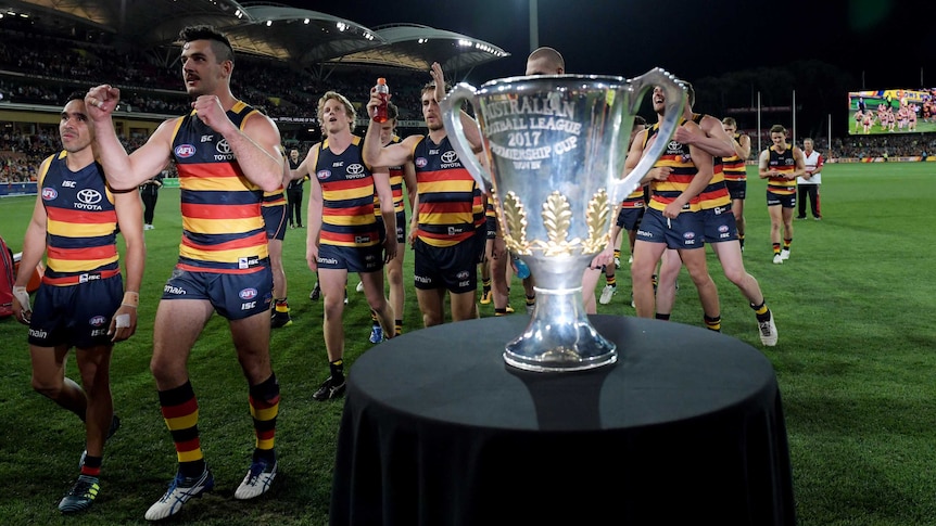 Crows players celebrate their prelim final win over Geelong as they walk next to premiership cup.