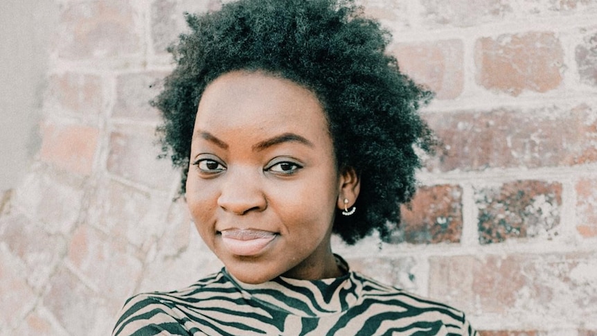 An African Australian woman poses a photo with her arms wrapped around her waist.