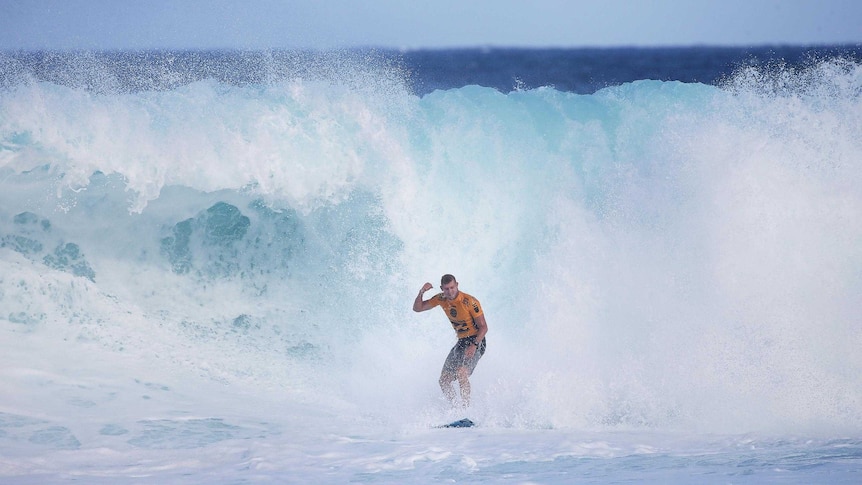 Mick Fanning stands up on his board and raises a fist as he celebrates his victory in the quarter-finals.