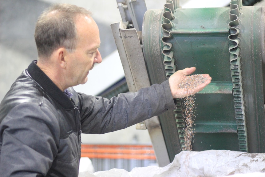 A man wearing a leather jacket pours a handful of plastic sprinkles into a container.