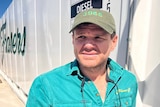 A man in a bright shirt leans up against a truck while fueling up. He looks concerned