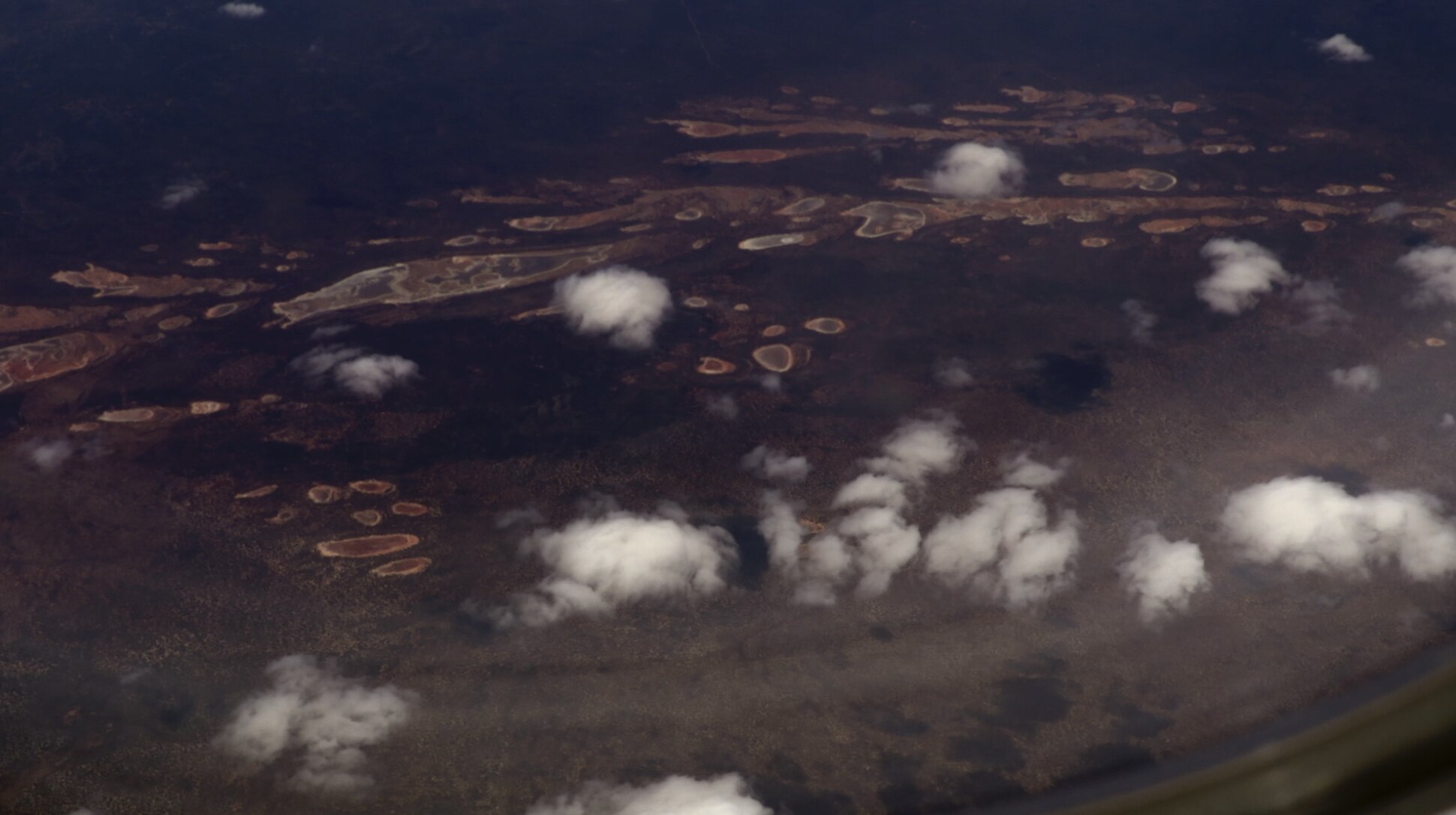 An aerial view looking down through wispy clouds above an arid landscape.