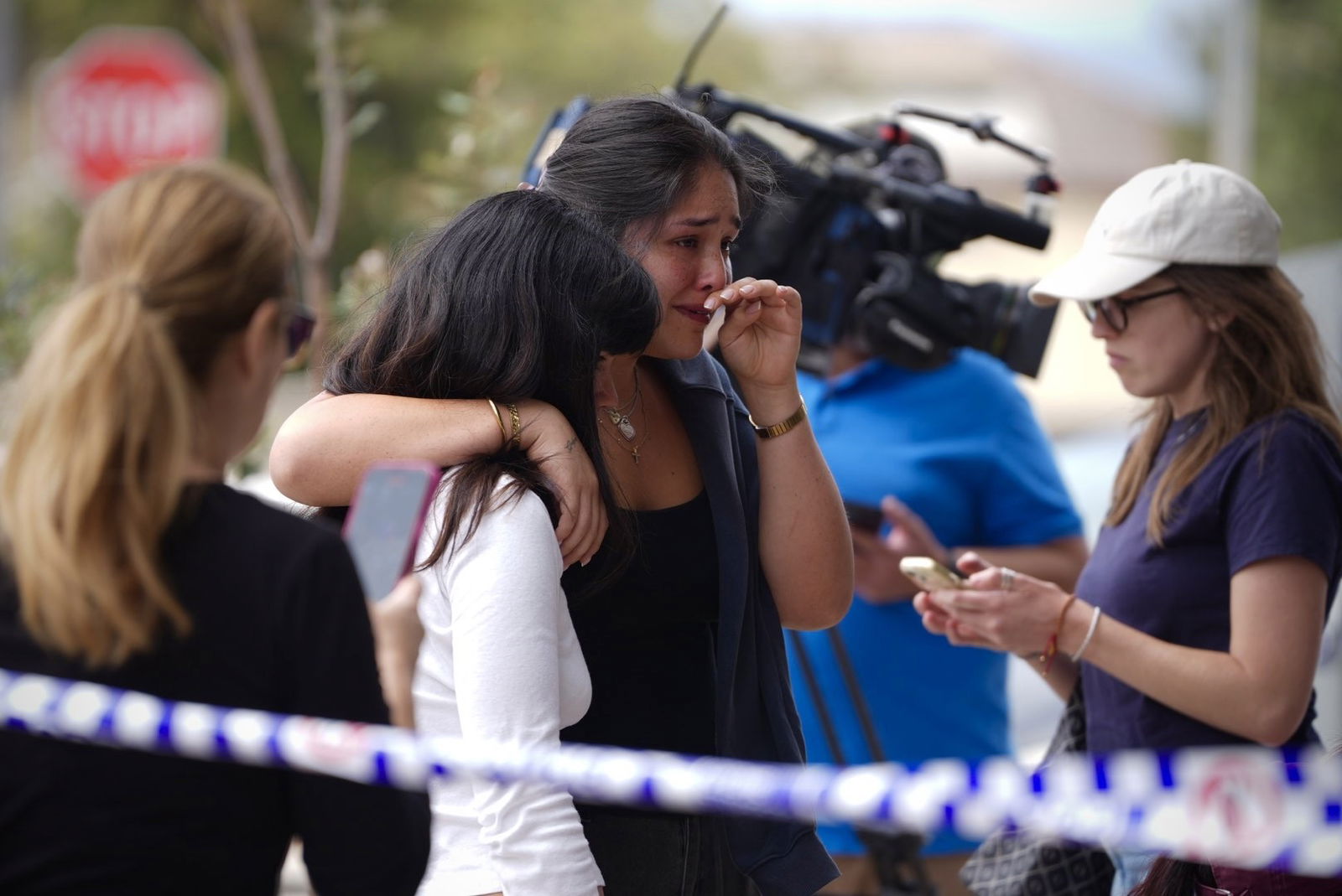 A young woman cries with her arm around another person, behind police tape