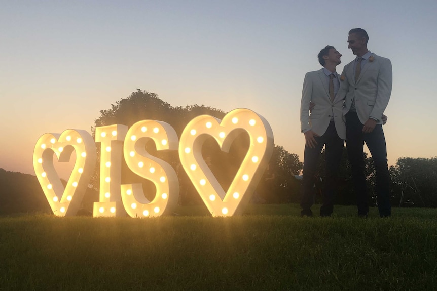 Craig Burns with his partner Luke Sullivan next to an illuminated "love is love" sign.
