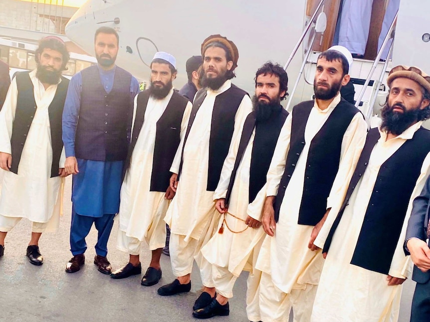 A group of Afghan men in traditional dress standing in front of a jet.