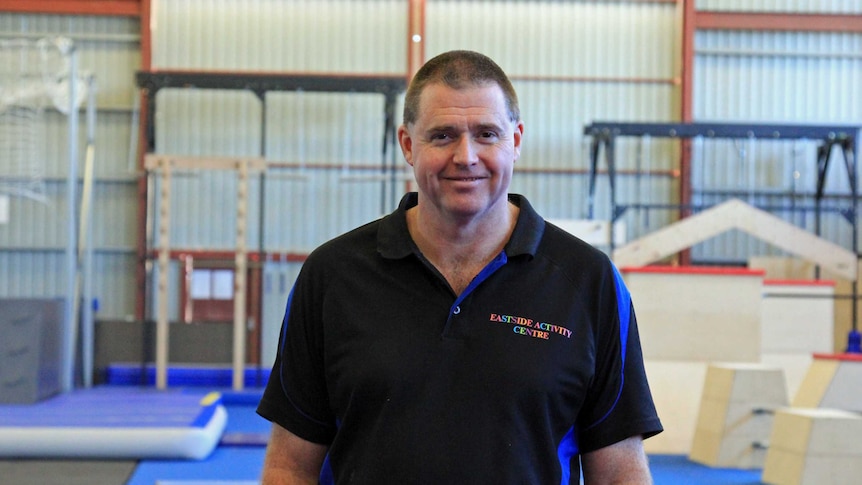 A man smiling standing in a large shed full of gymnasium equipment