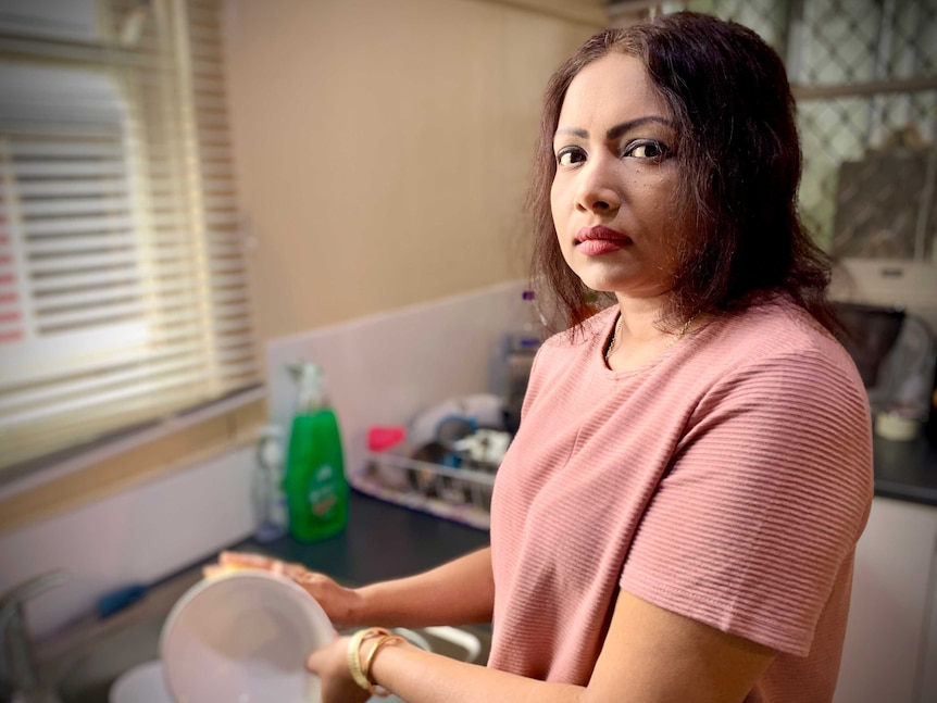 A woman wearing a pink shirt does the dishes.