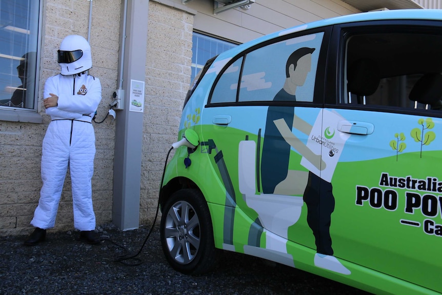 The Stink stands with arms crossed behind Queensland Urban Utilities' poo-powered car while it fills up