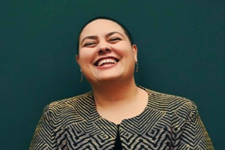 A woman in a blazer smiles in front of a dark turquoise background, and reflects on her dating life.