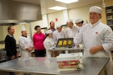 Glossop High School student Zoe Harrington stands with a tray of pastries in front of fellow students and staff.
